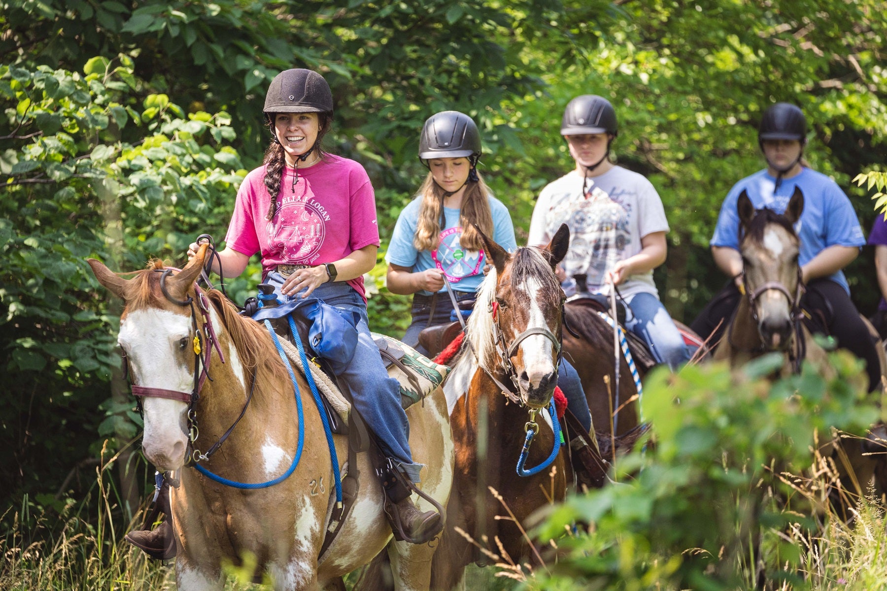 A group of Girl Scouts rides on horseback through the woods