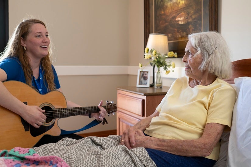 A musical therapist plays a song on the guitar for an elderly female patient.