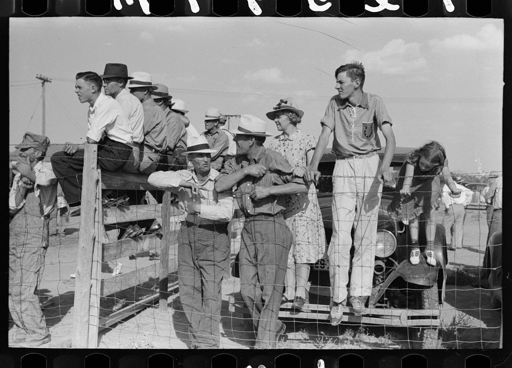 A group of adults and children sit and stand by a fence at a 1940's 4-H fair