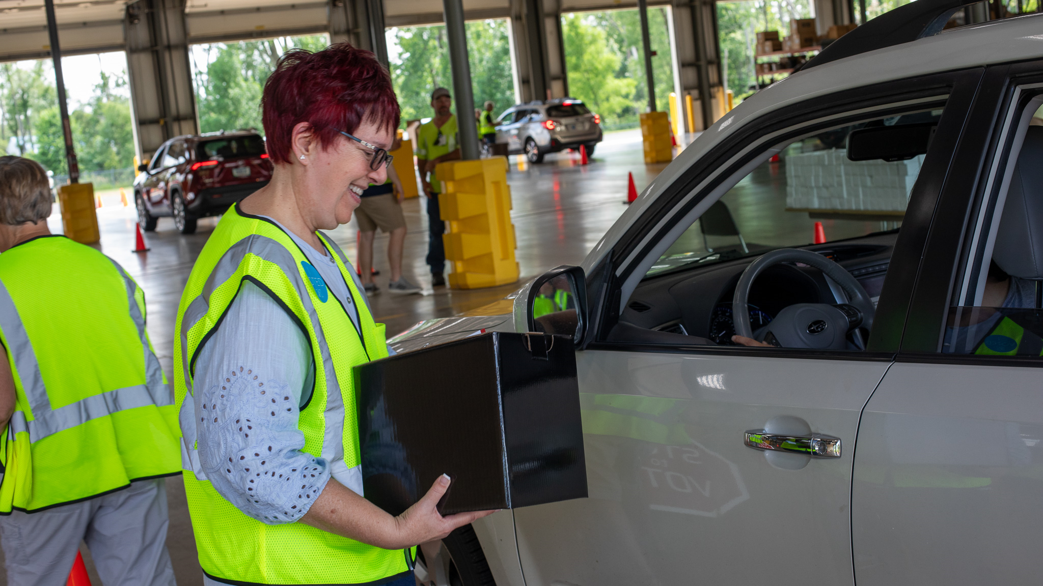 Altrusa volunteer Carol Vierling holds a ballot box as she talks with a KREMC member at the drive-through annual meeting.