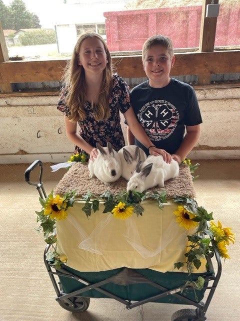 Ella Jarrett stands with another 4-H participant in front of some rabbits. 