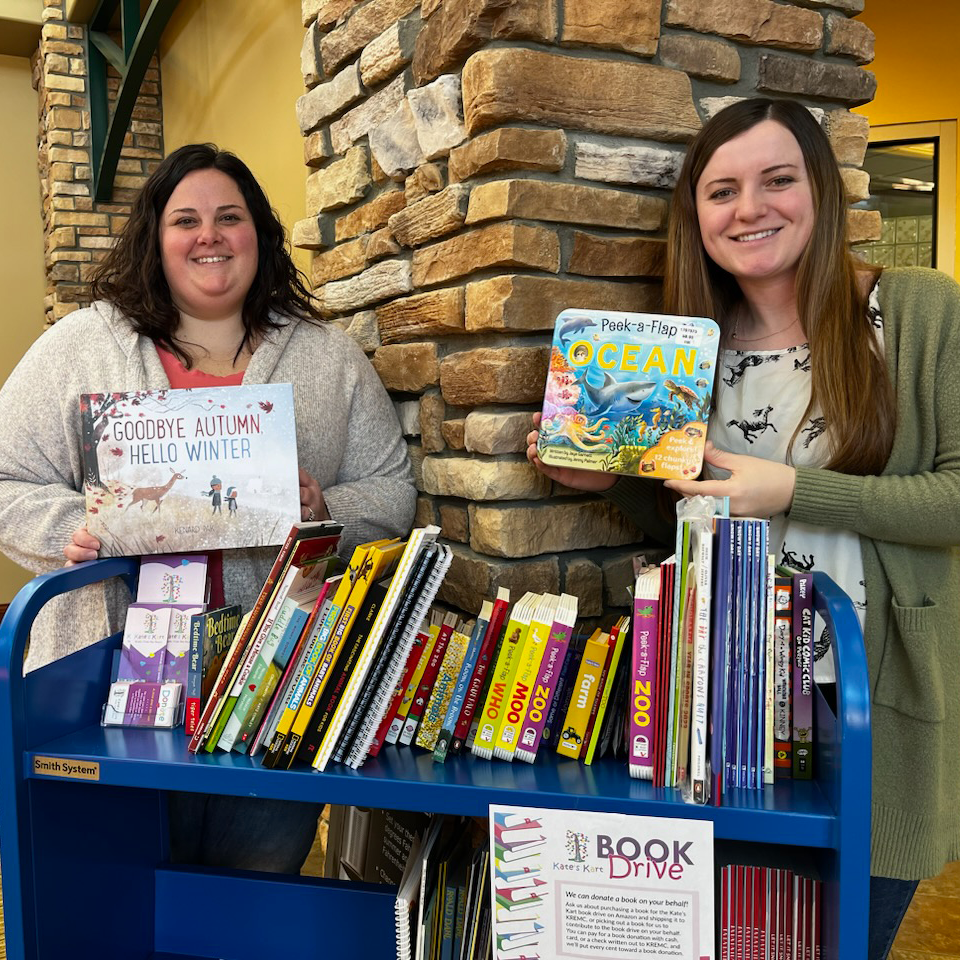 Two KREMC employees standing by book cart in lobby