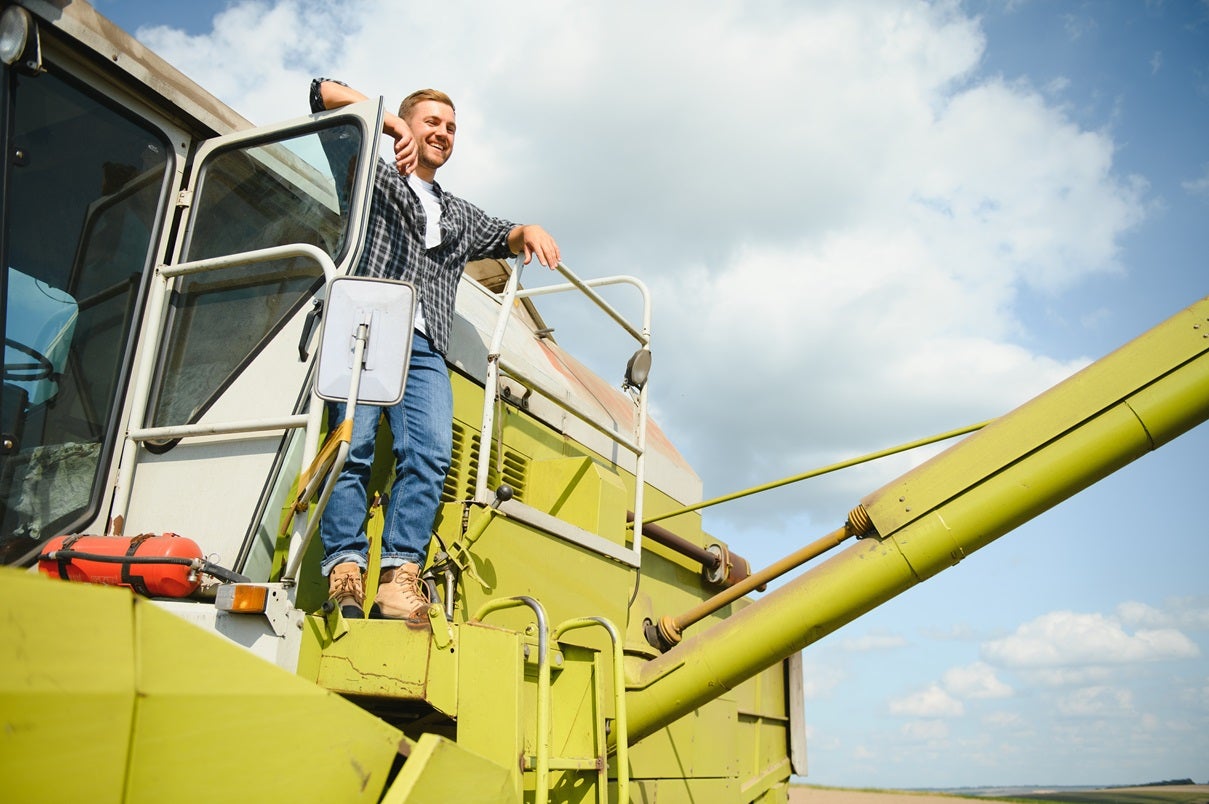 A farmer stands on his tractor smiling while he looks out into the field.