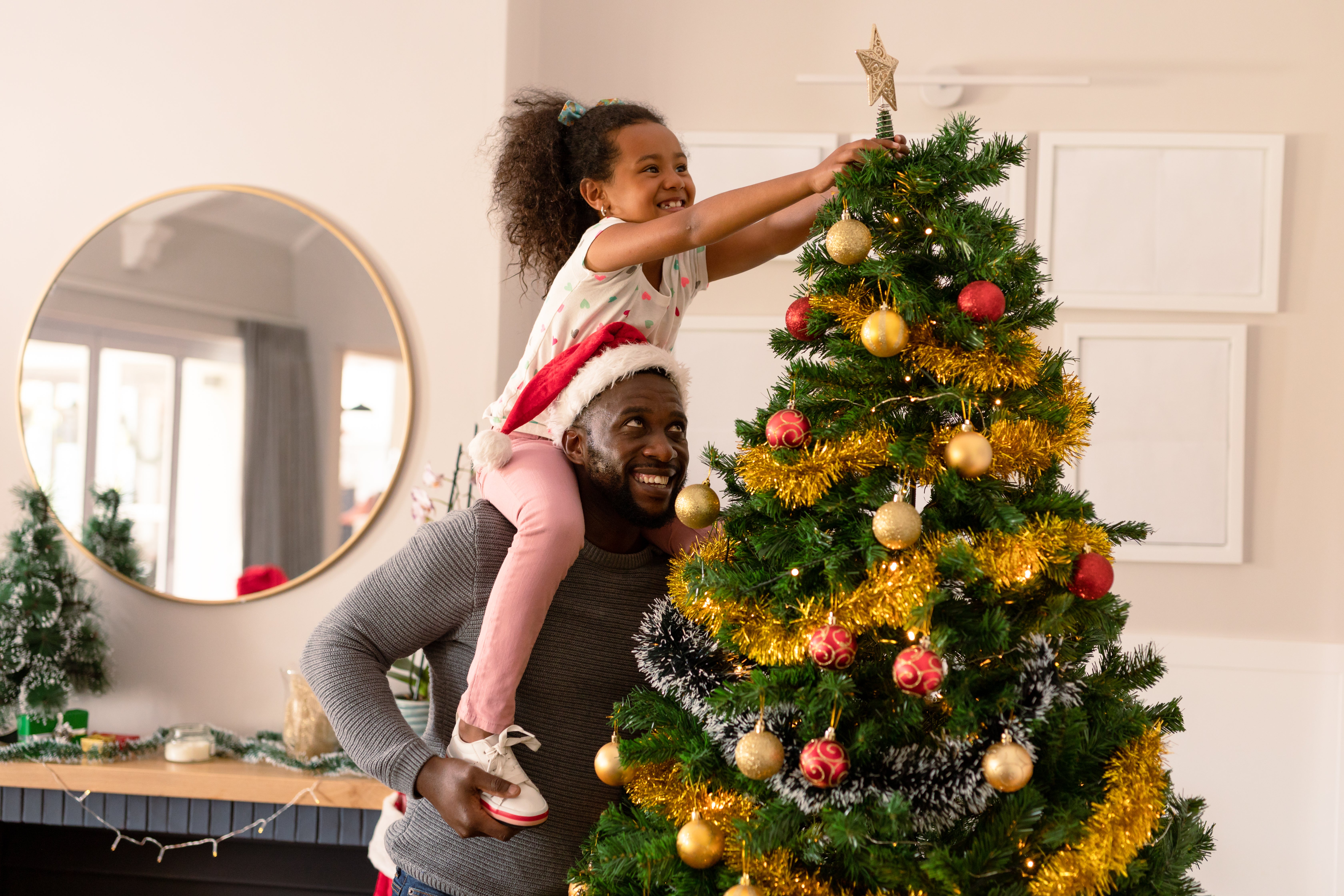 Father holding daughter on his shoulders to decorate Christmas tree