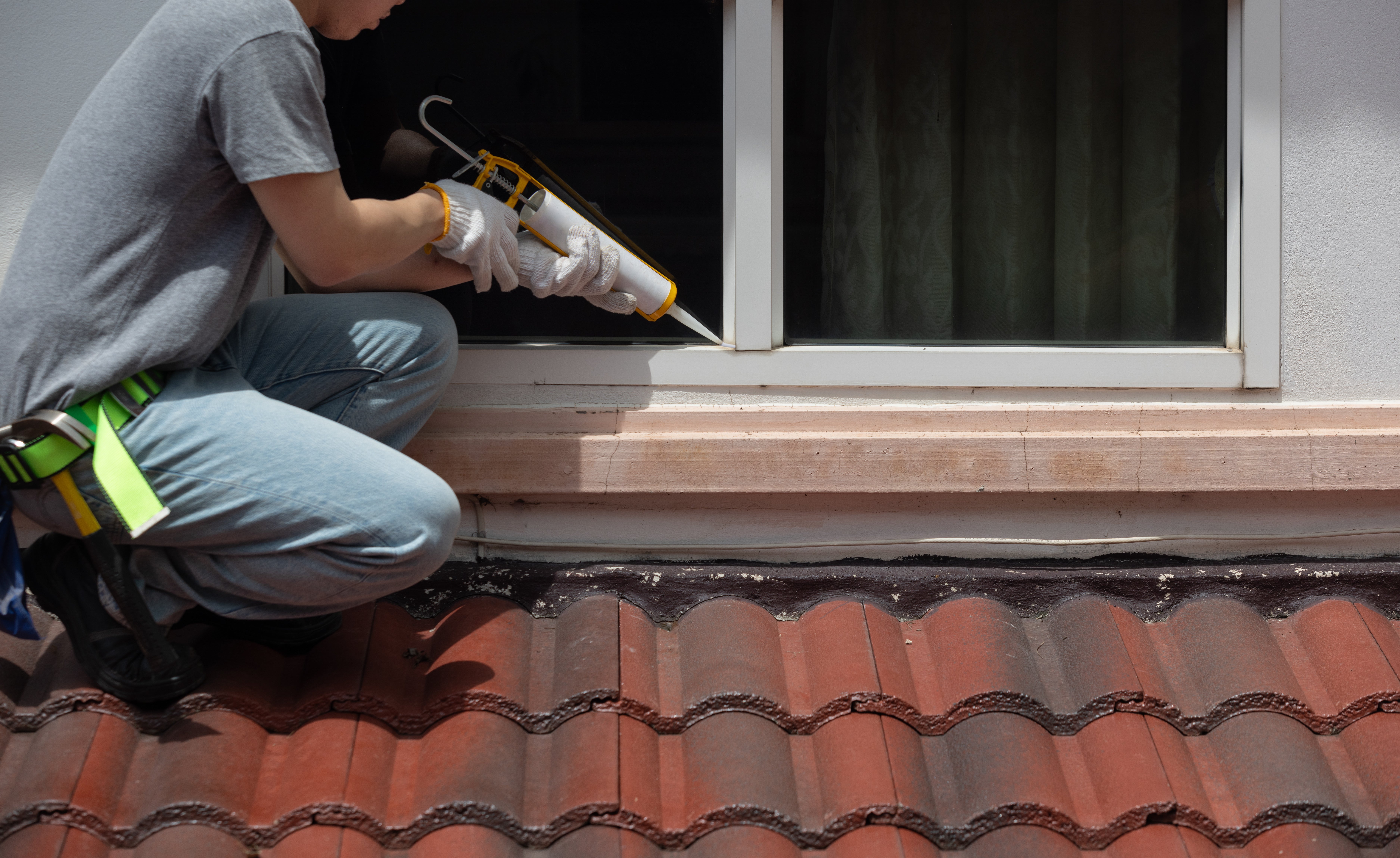 Man sealing window with caulk