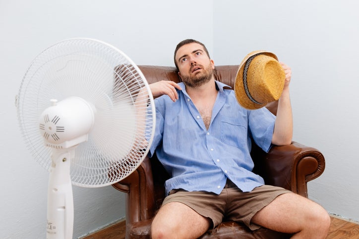 A man sits stretched out in front of an oscillating fan.