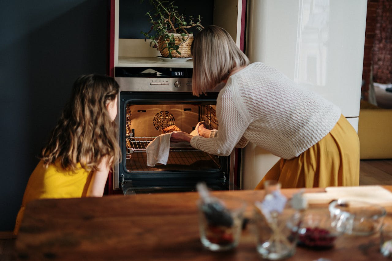 A woman and child look at baked good inside of an oven.