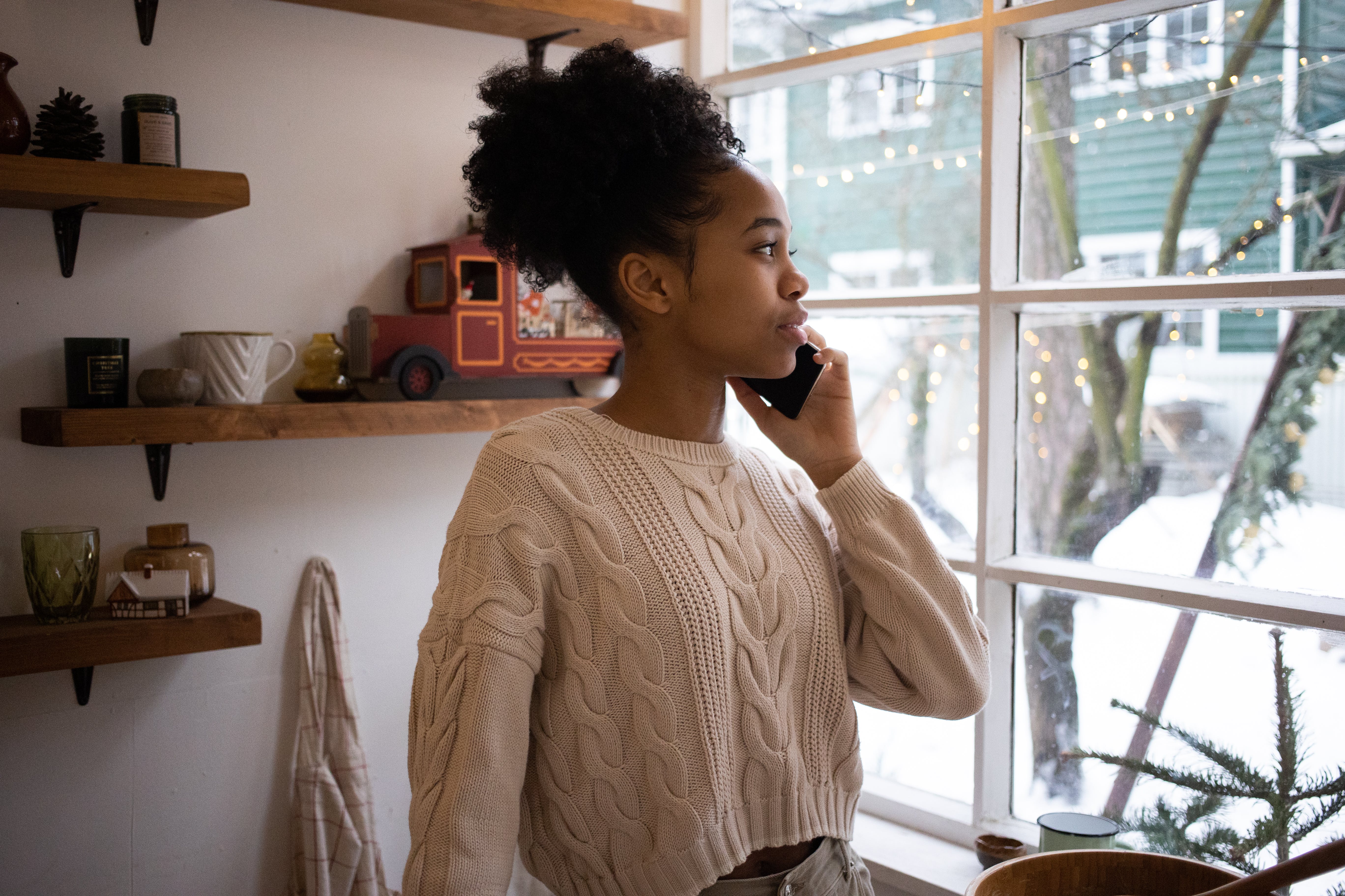 A woman stands in front of a window while talking on the phone.