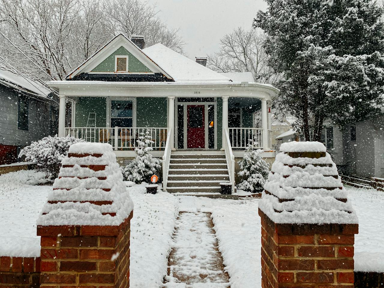 Snow falls in town on a charming, green home.