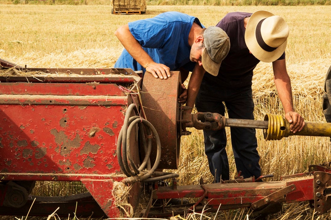 Two men are bent over, working on a tractor.